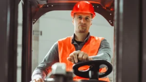 Operator w pomarańczowym kasku i kamizelce odblaskowej za kierownicą wózka widłowego