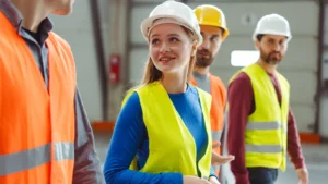 Czworo pracowników w kaskach i kamizelkach odblaskowych we wnętrzu hali, w tle sprzęt przeciwpożarowy